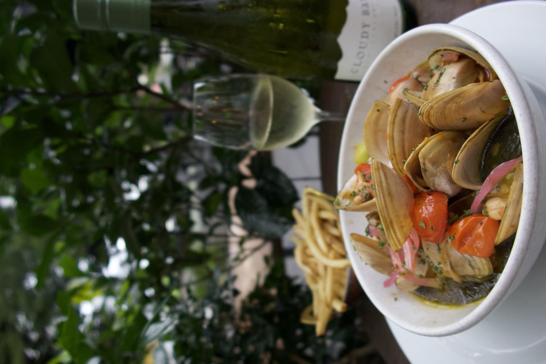 Bowl of Diamond Shell clams in broth with cherry tomatoes, served with white wine