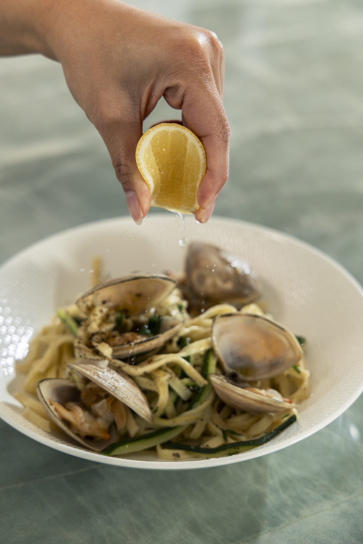 Squeezing lemon over linguine with Diamond Shell clams and zucchini