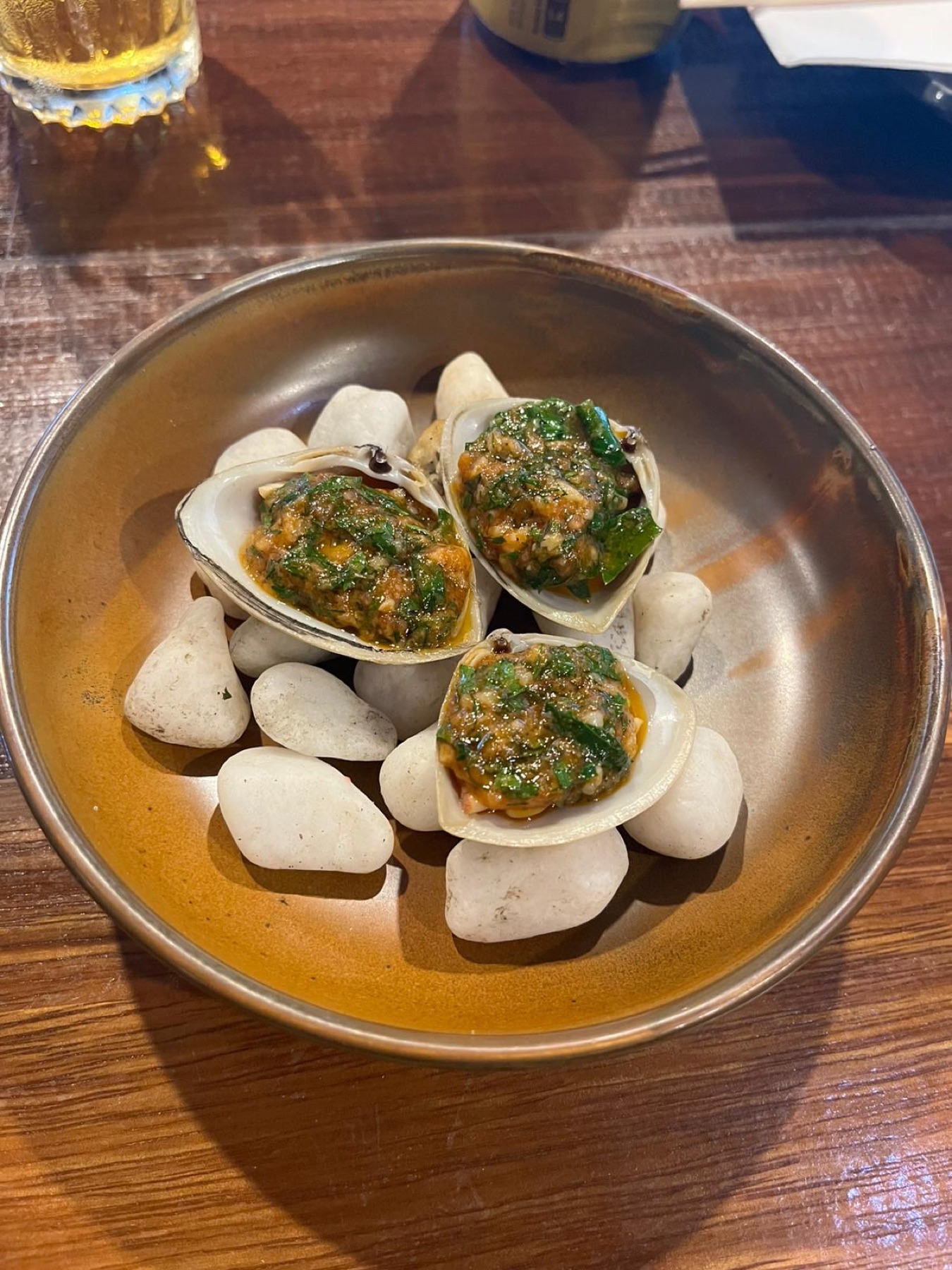 Tuatua clams on the half shell topped with a green herb and garlic dressing, served on river stones